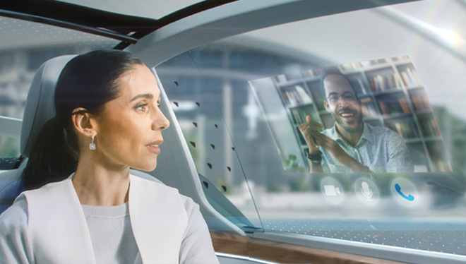 Woman sitting in autonomous vehicle chatting on a VR video conference screen overlaid on the car window.